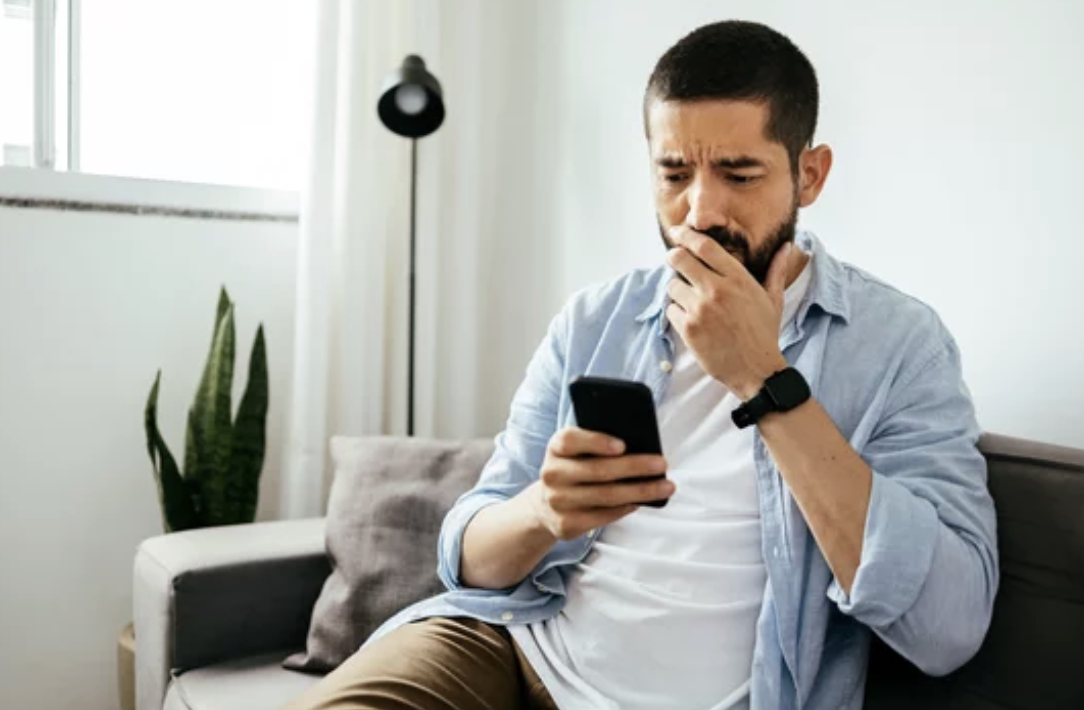 Adult man with a concerned face and looking at his phone texting 741741 for free mental health support.